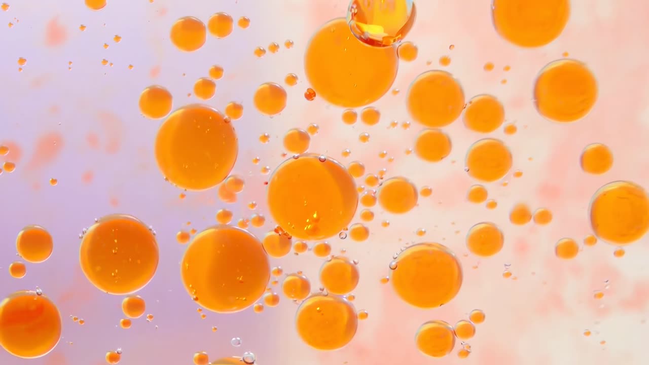 オレンジ色の泡が浮かぶ抽象的な動画。パステルカラーの背景を真上からのアングルで捉えたライブ映像。