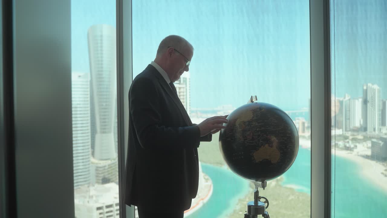 Senior businessman in a high-rise office with a stunning view of the city uses a globe as he considers his next business plan