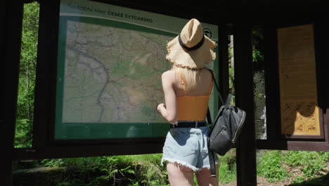 detrás de una joven mirando el mapa del parque nacional bohemio de suiza, república checa en un día soleado