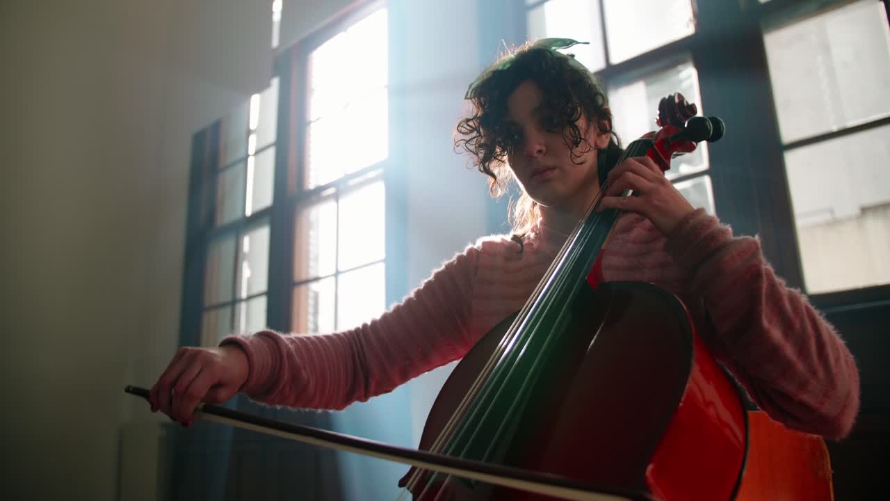 Young Woman Playing Cello with Sheet Music in a Backlit Room
