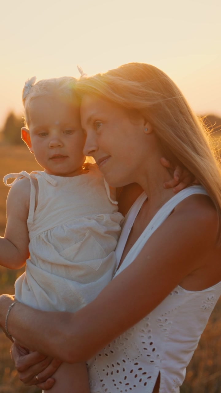 Mutter hält ihre kleine Tochter in einem goldenen Weizenfeld bei Sonnenuntergang