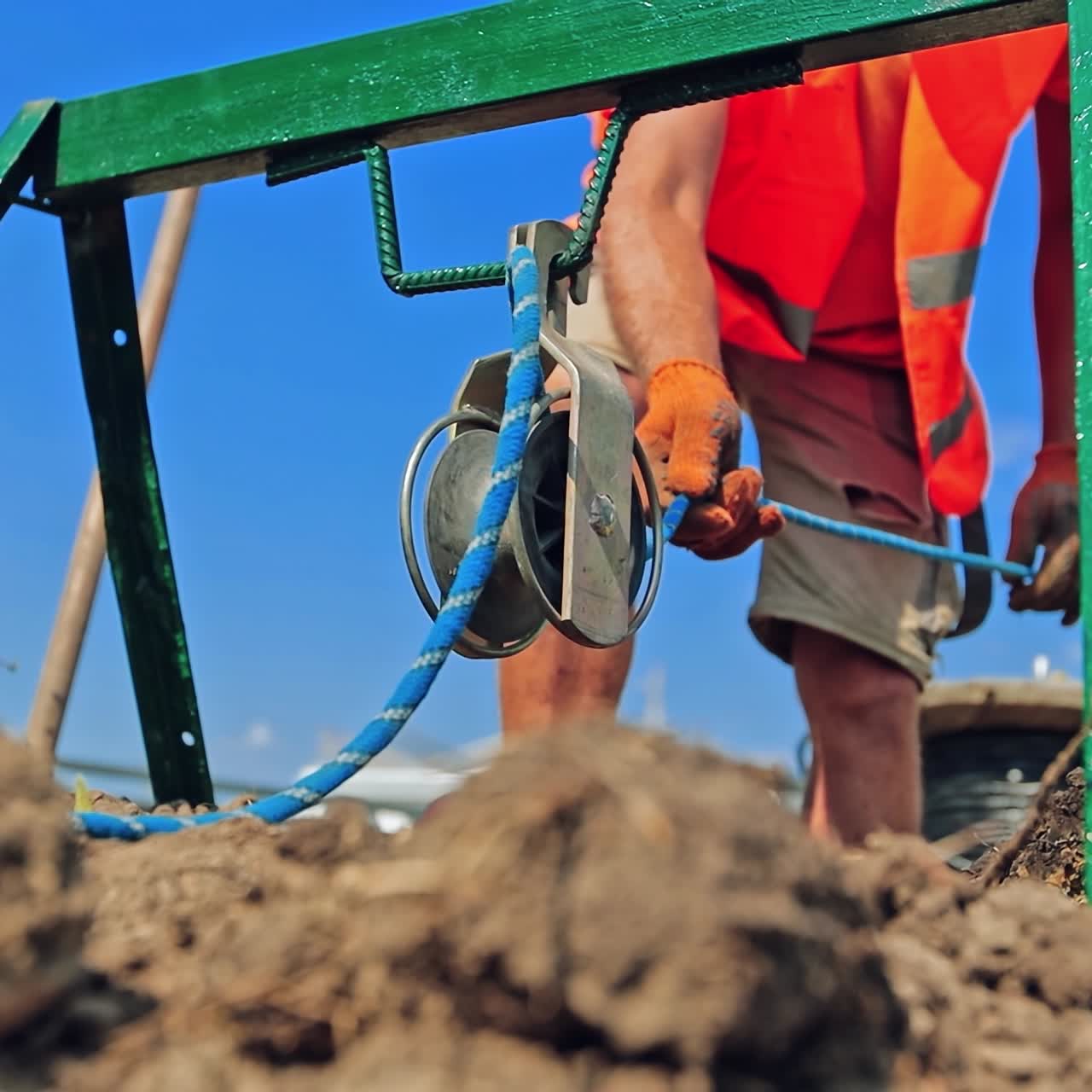 Engineering works against blue sky. Worker uses rope during construction outdoors. Equipment for building.
