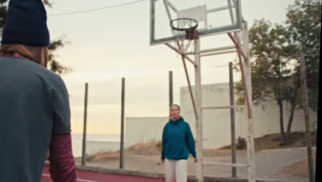 shot from behind a blonde girl with a bob hairstyle receives a basketball, catches it and throws it into the basketball hoop while playing with her friend on a summer morning