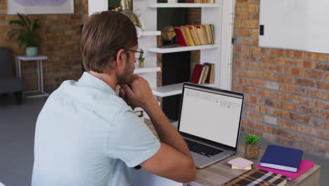 hombre caucásico sentado en el escritorio viendo el procesamiento de datos de codificación en la pantalla del portátil
