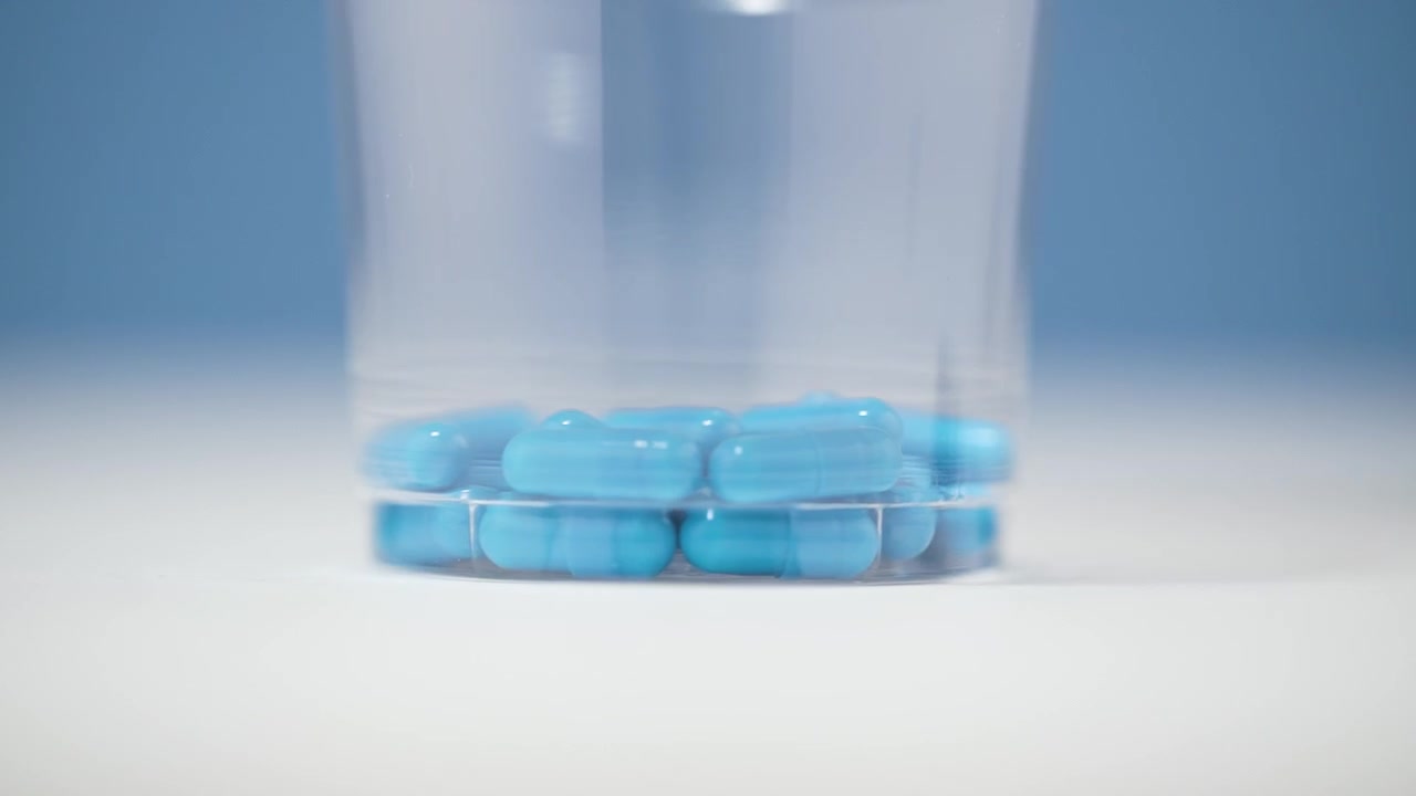 Primo piano di pillole mediche blu in una capsula trasparente di plastica, posizionate su una superficie bianca, con sfondo sfocato.