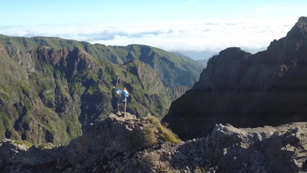 Splendida ripresa grandangolare con drone di un singolo escursionista che percorre un drammatico sentiero su cresta montuosa vulcanica a Madeira, Portogallo. Caratterizzato da imponenti cime rocciose, valli profonde e un'ampia luce mattutina
