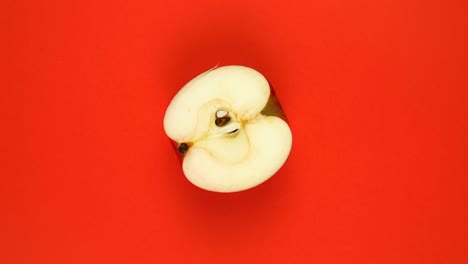 top view: half of an apple rotates on a red surface - slow motion