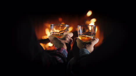 hands of two men with glasses of whiskey on the background of the fireplace male rest