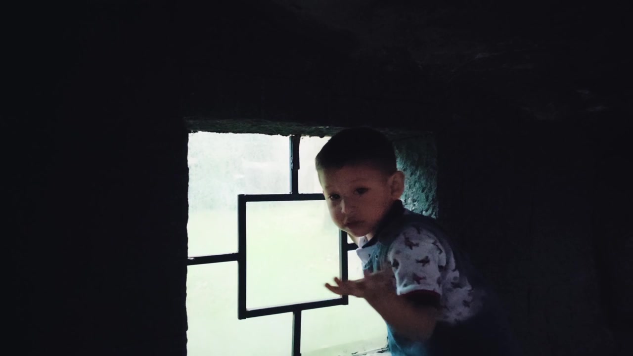 A curious 2-year-old white boy peeks out from a small, dark window of a miniature observatory, intently looking for animals in the zoo.