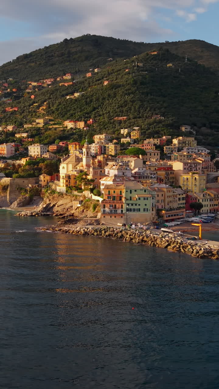 Panoramica aerea verticale di una colorata città costiera e del porto sulla Riviera Italiana al tramonto.
