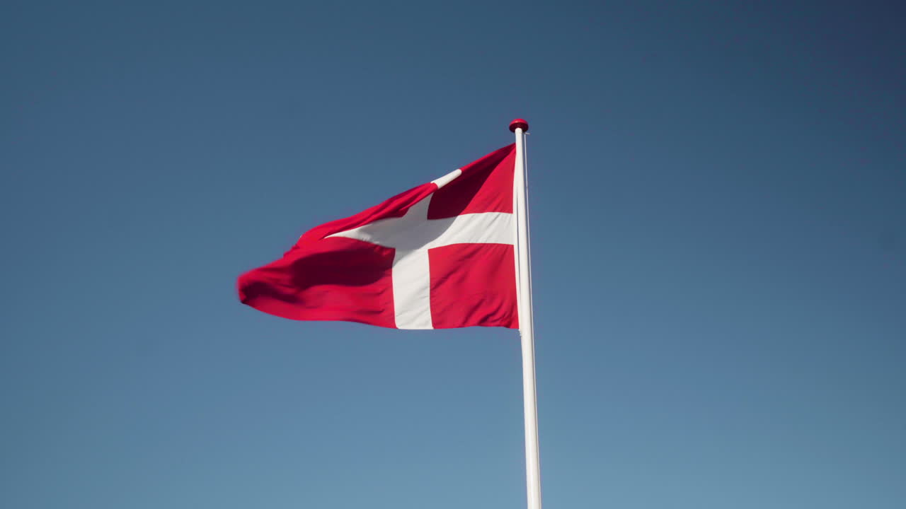 Danmarks flag blafrer i vinden i slow motion, nærbillede med blå himmel i baggrunden
