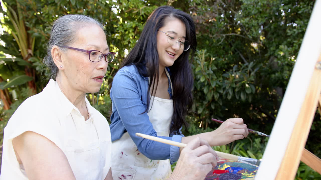 Painting together outdoors, asian grandmother and granddaughter enjoying painting on canvas
