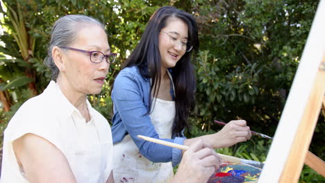 painting together outdoors, asian grandmother and granddaughter enjoying painting on canvas