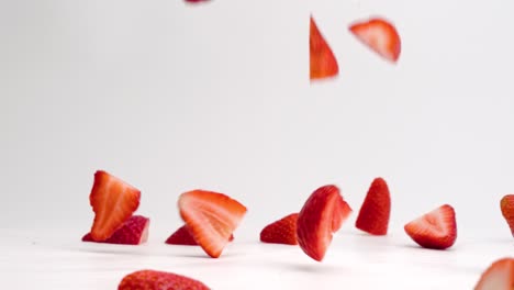 Fresh,-bright-red-sliced-halved-strawberries-falling-and-bouncing-into-a-pile-on-white-table-top-in-slow-motion