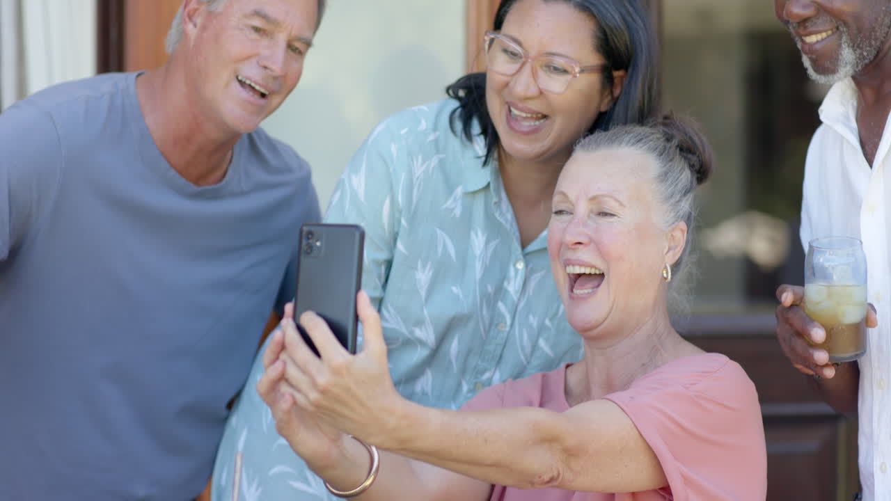 Senior woman laughing with diverse senior friends while looking at smartphone in garden
