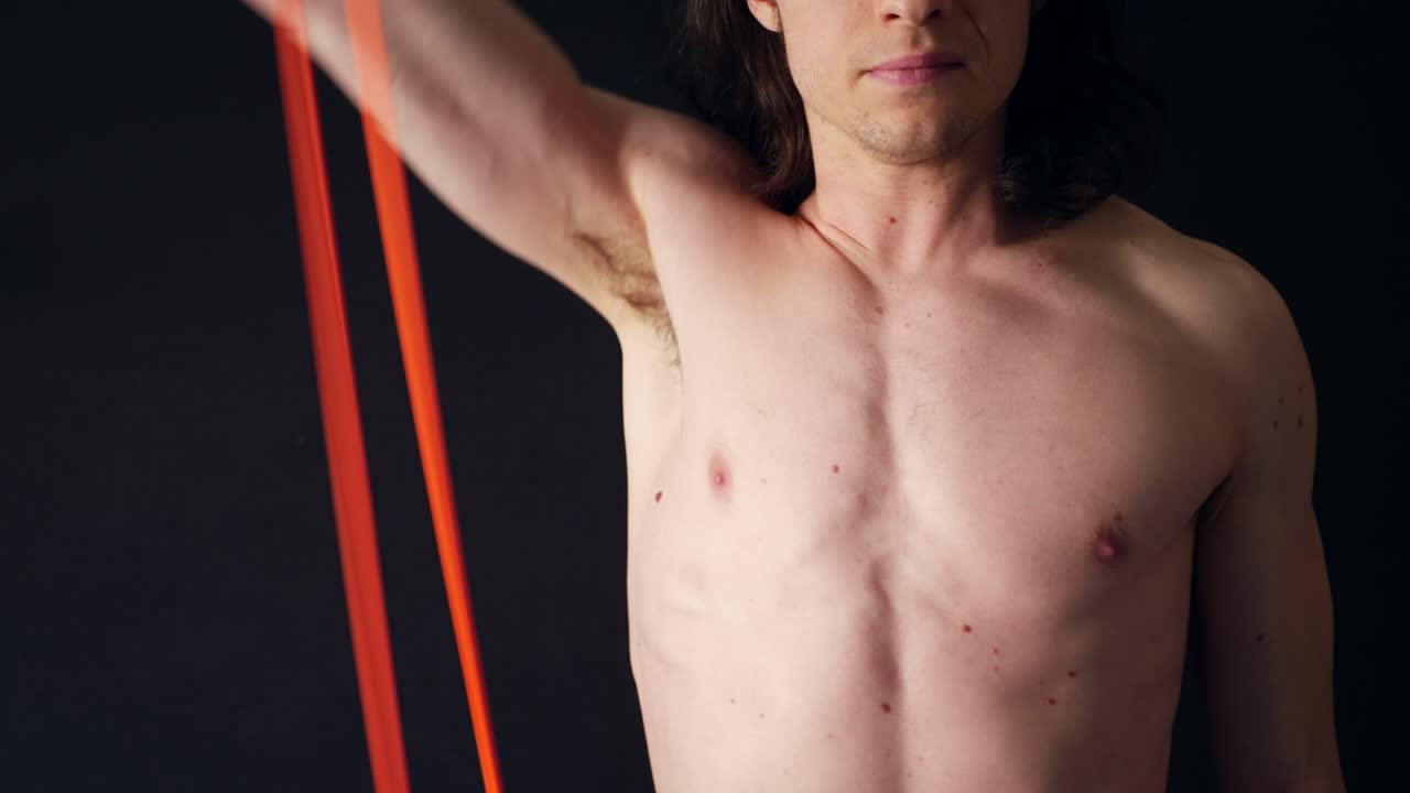 체육관 슬로우 모션에서 저항 밴드 운동으로 어깨 삼각근을 훈련하는 강한 셔츠 없는 백인