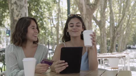 mujeres jóvenes alegres que pagan con tarjeta de plástico a través de una tableta