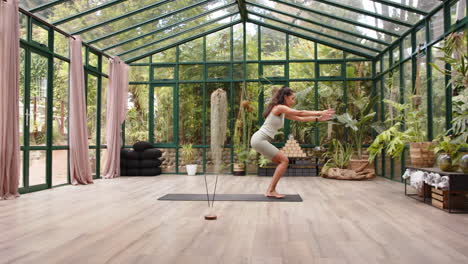 practicing yoga, woman performing chair pose on mat in glass house, copy space