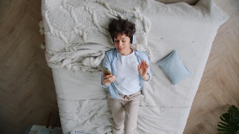 woman relaxing on bed, listening to music and using phone