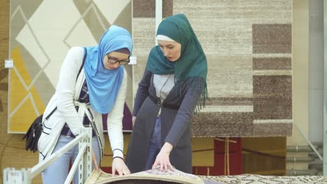 two young muslim women in hijab choose a rug in the store