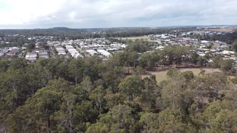 drone flying over bushland towards a green field and residential estate in the background