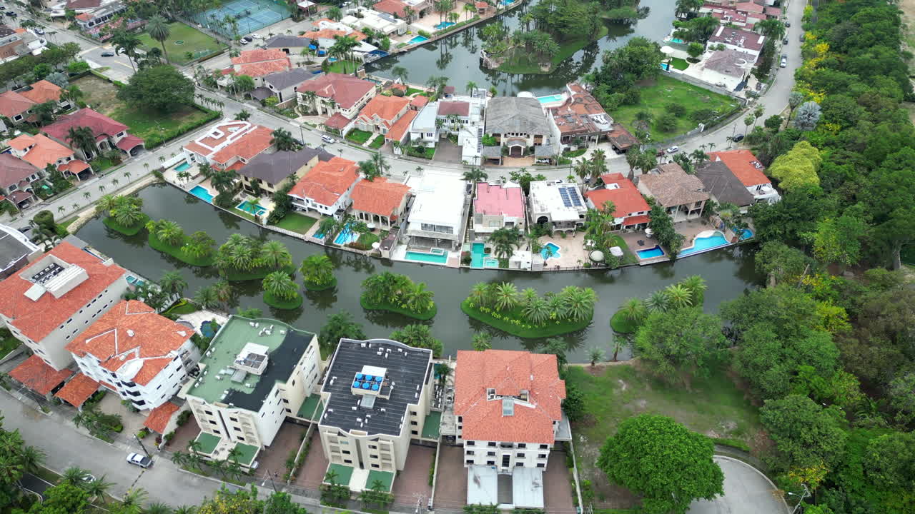 Aerial shot captures the beauty and exclusivity of a gated community on Via a la Costa, Guayaquil, Ecuador. Residences, surrounded by lush vegetation and water canals, create a harmonious landscape.