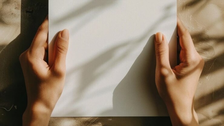 Hands holding paper with leaf shadows, captured from above