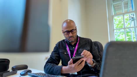 Focused-businessman-seated-at-a-desk-using-his-smartphone-in-a-modern-office-environment-during-work