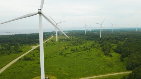 aerial drone footage ascending and flying higher in front of tall white colored renewable energy creating wind turbines at a wind farm in pakri peninsula during a cloudy day. turbines spinning slowly