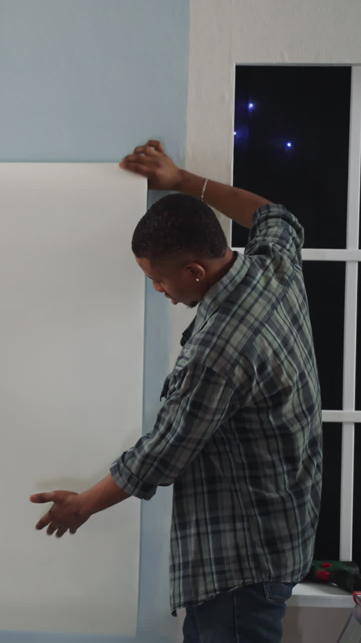 African-American men discuss wallpaper choice putting sheet on wall in flat. Black designers seek decision for house decoration. Home renovation problems