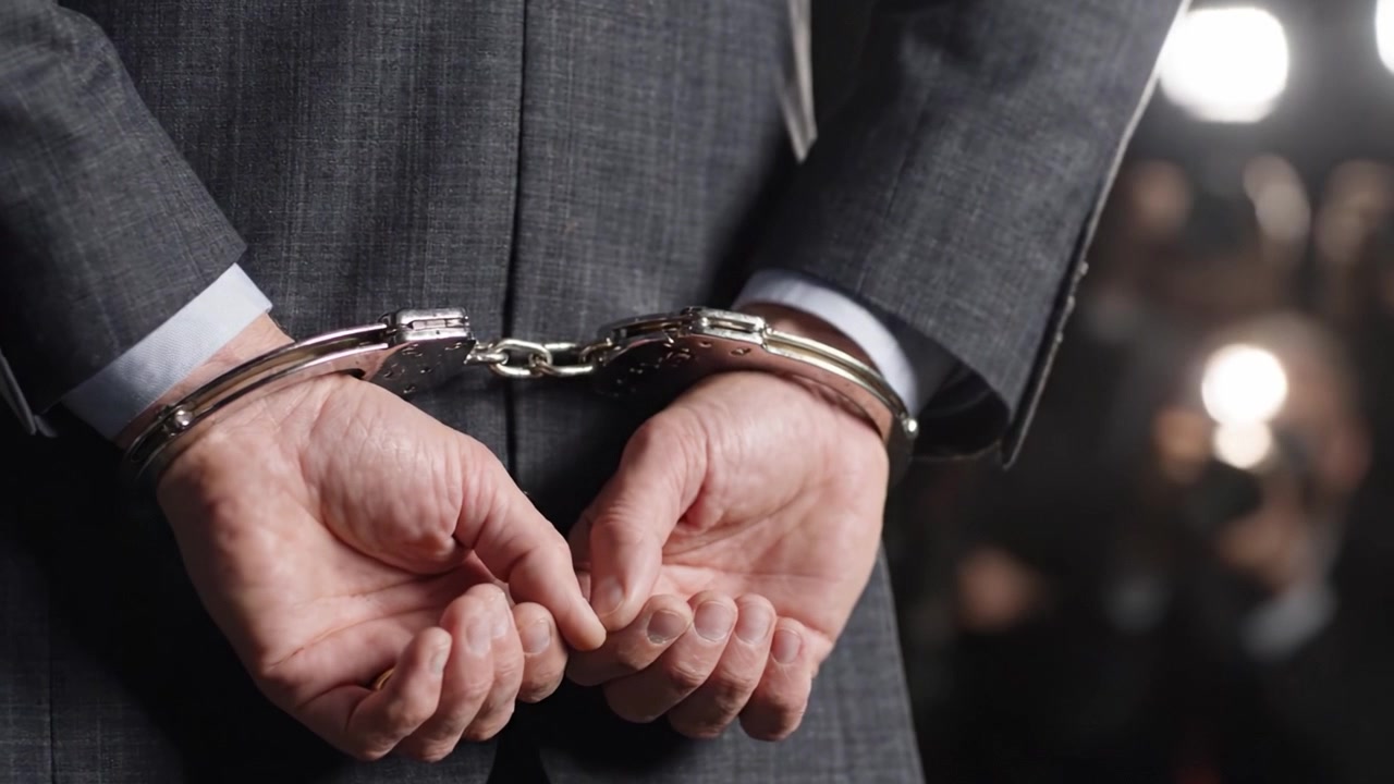 En dyster scene fanger en mand i jakkesæt med hænderne lænket bag ryggen, der viser de alvorlige konsekvenser af kriminalitet og retfærdighed i et miljø med høje indsatser.