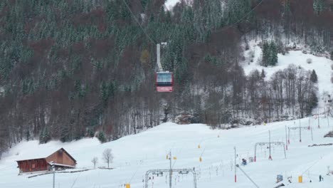 cable cars moving down the snowy mountain slopes as tourists are skiing below at a mountainside located in engelberg in brunni, switzerland