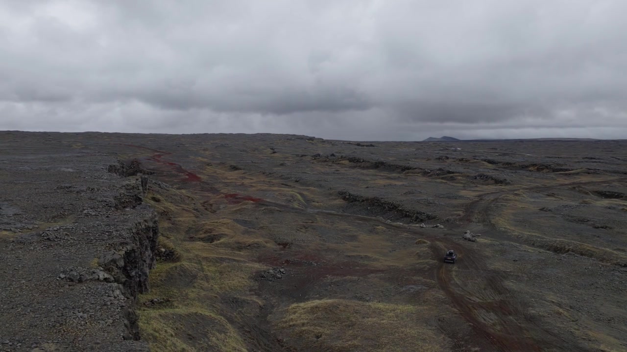 Car traveling across fractured volcanic terrain on the Reykjanes Peninsula, Southwest Iceland, within the North American and Eurasian plate boundary landscape, drone slide and tracking shot.