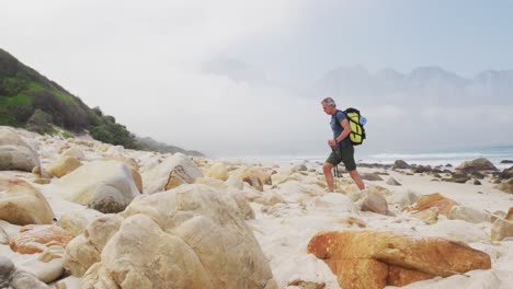 senior hiker man with backpack and hiking poles walking while hiking on the beach.