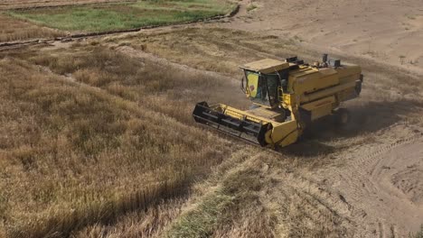 aerial view of yellow combine harvester turning in rural punjab field