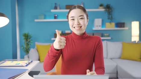 asian woman is pleased with what she sees on laptop and gives a positive sign to the camera.