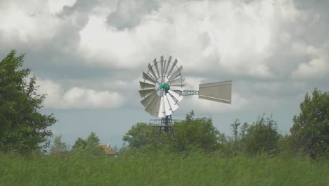 Antiguo-Molino-De-Viento-Americano-Holandés-Cerca-Del-Agua-Y-La-Caña,-Un-Pequeño-Carro-Rodado-En-Cámara-Lenta-Girando-En-El-Viento