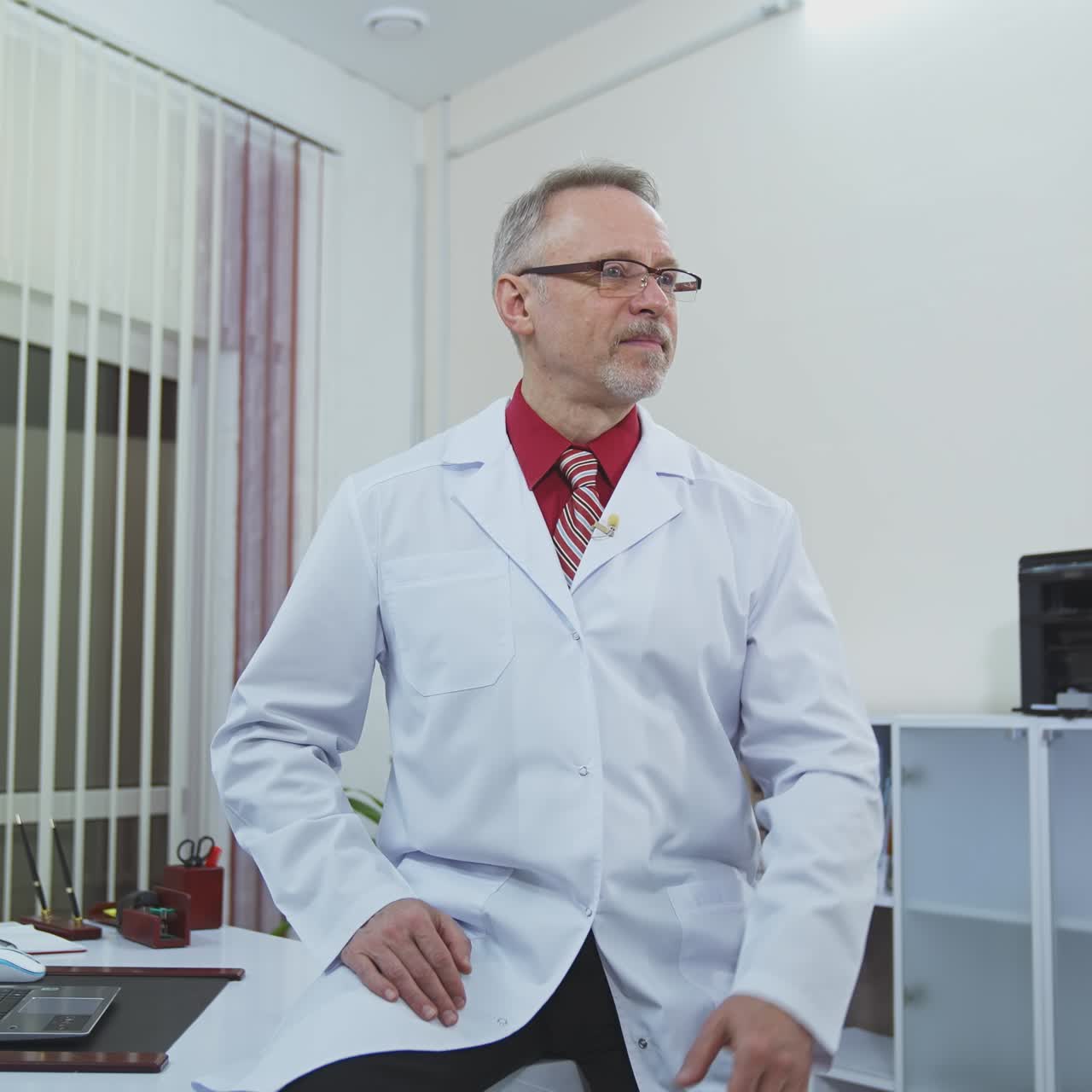 Smiling doctor sitting at his desk in his office. Doctor is working in his medical office