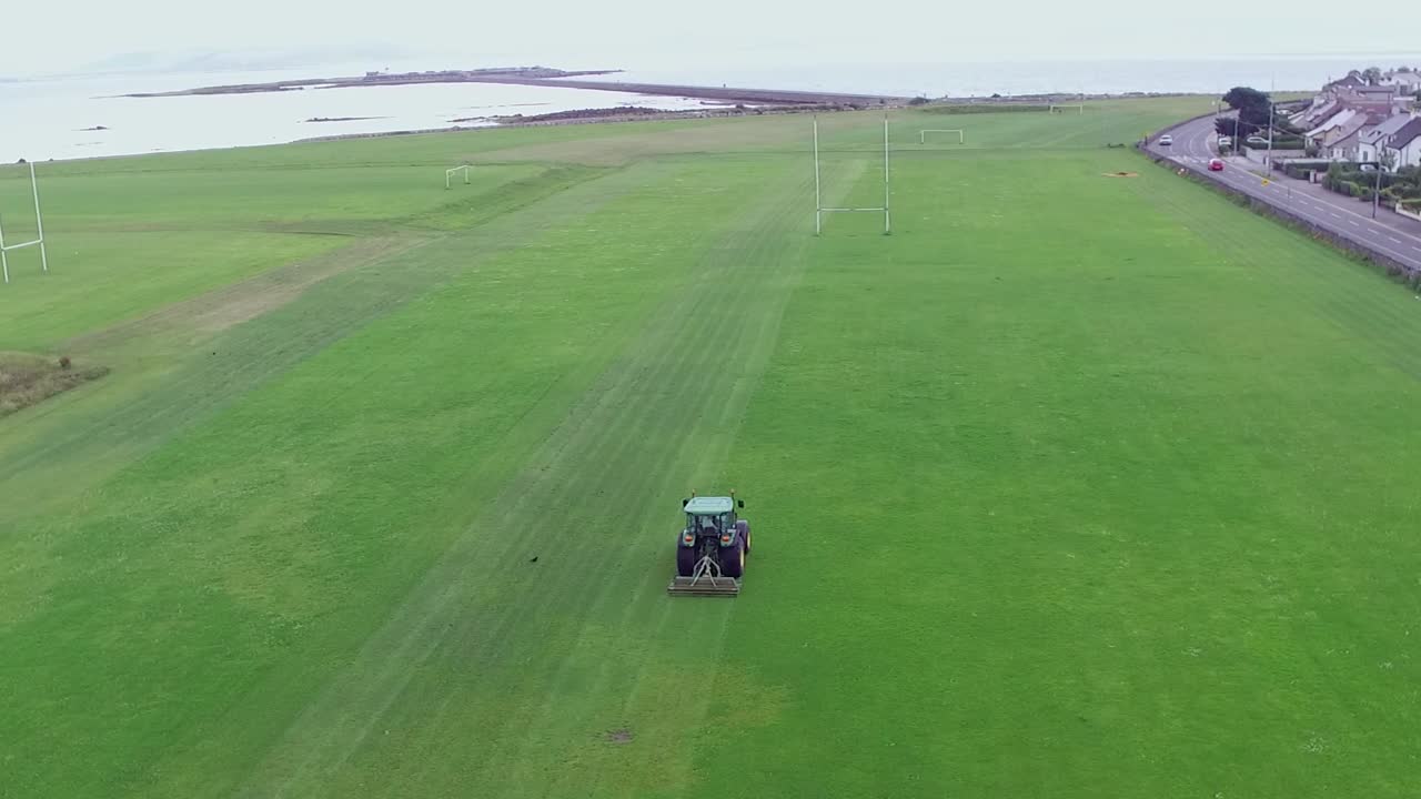 fotografía aérea de un tractor en el cladddagh, ciudad de galway, irlanda cortando el césped en un campo de gaa con el océano en el fondo