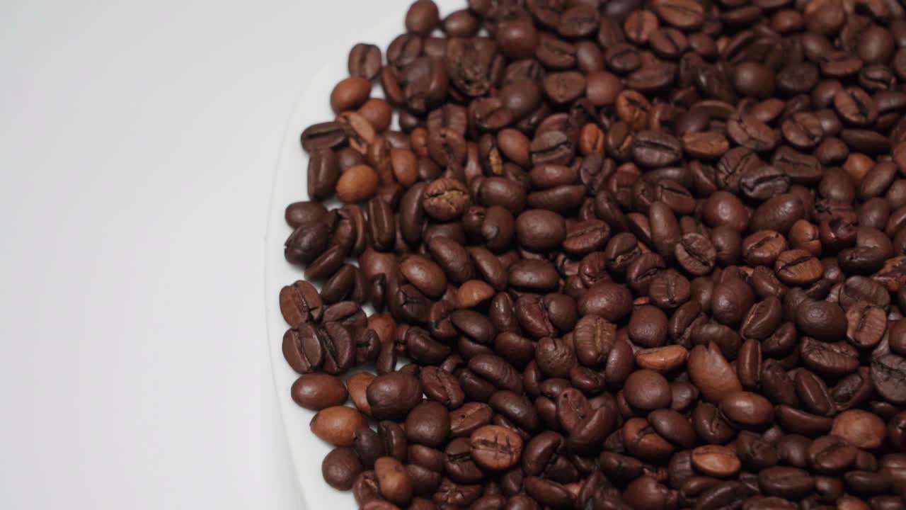 Chicchi di caffè in rotazione su sfondo bianco con spazio per il testo a sinistra, vista dall'alto