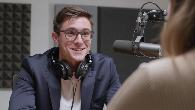 Responding to interviewer cue host in navy blazer smiling chuckling at studio with boom mic headset