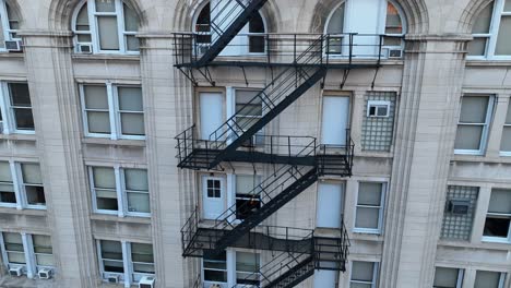 Aerial-shot-of-a-classic-stone-building-facade-with-ornate-architectural-details,-showcasing-rows-of-arched-windows-and-exterior-fire-escapes