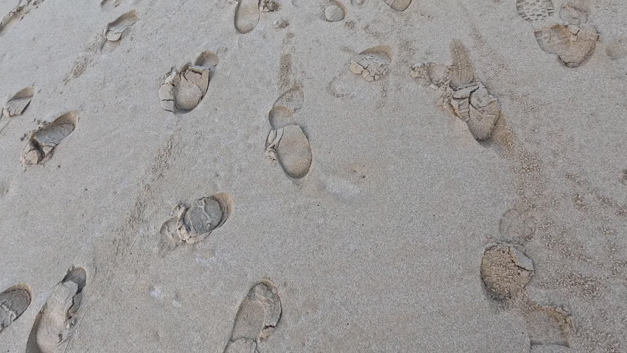 huellas de zapatos esparcidas por la playa de arena.