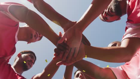 animation of confetti falling over male football team stacking hands on pitch