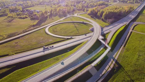 slow drone orbit reveals katlakalns a5 riga bypass interchange showing loop ramp, overpass bridge, daugmale road, vehicles flow on grade-separated lanes under afternoon light, springtime