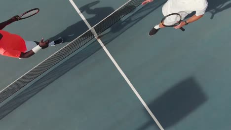 Diverse-male-tennis-players-holding-rackets-and-shaking-hands-at-court