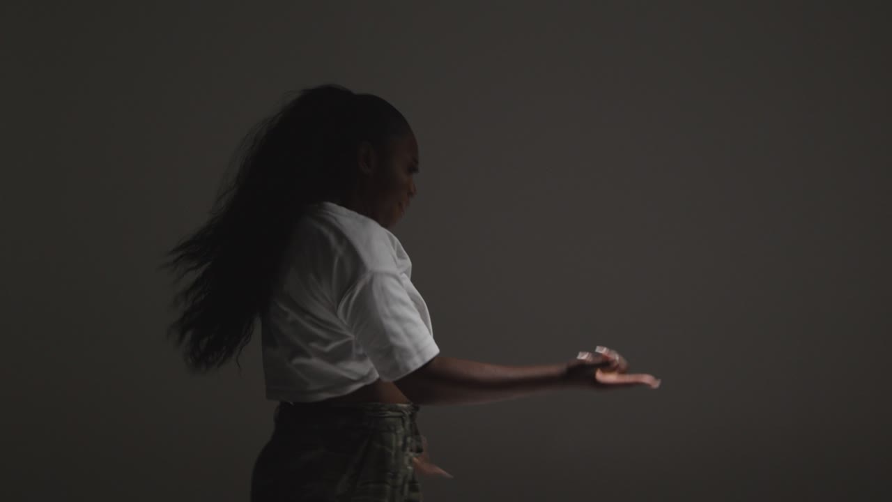 Profile Studio Shot Of Young Woman Dancing With Low Key Lighting Against Grey Background