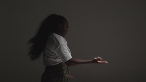 Foto-De-Estudio-De-Perfil-De-Una-Mujer-Joven-Bailando-Con-Iluminación-Discreta-Sobre-Fondo-Gris