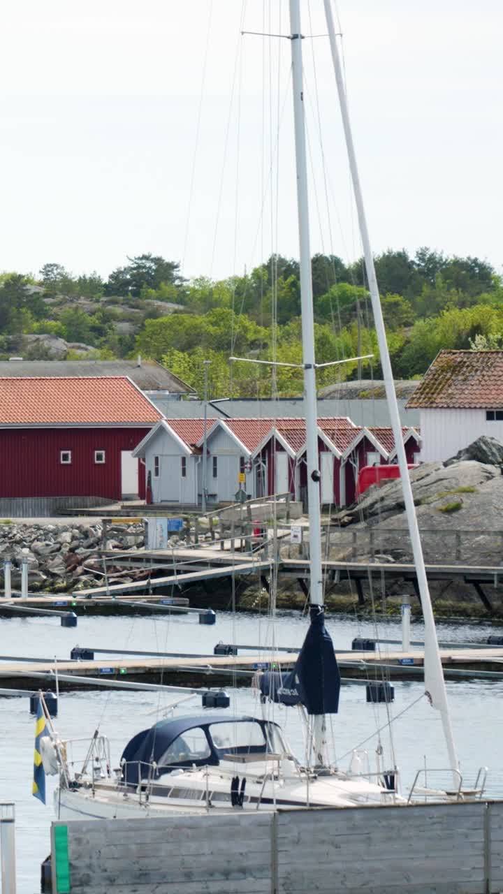 Vertical, aerial: Swedish sailing boat in a harbor during the day with red houses in Sweden, establishing drone shot