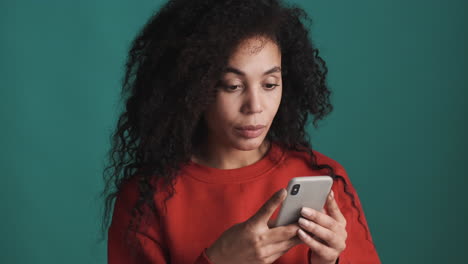 una mujer afroamericana usando un teléfono inteligente sobre un fondo azul.